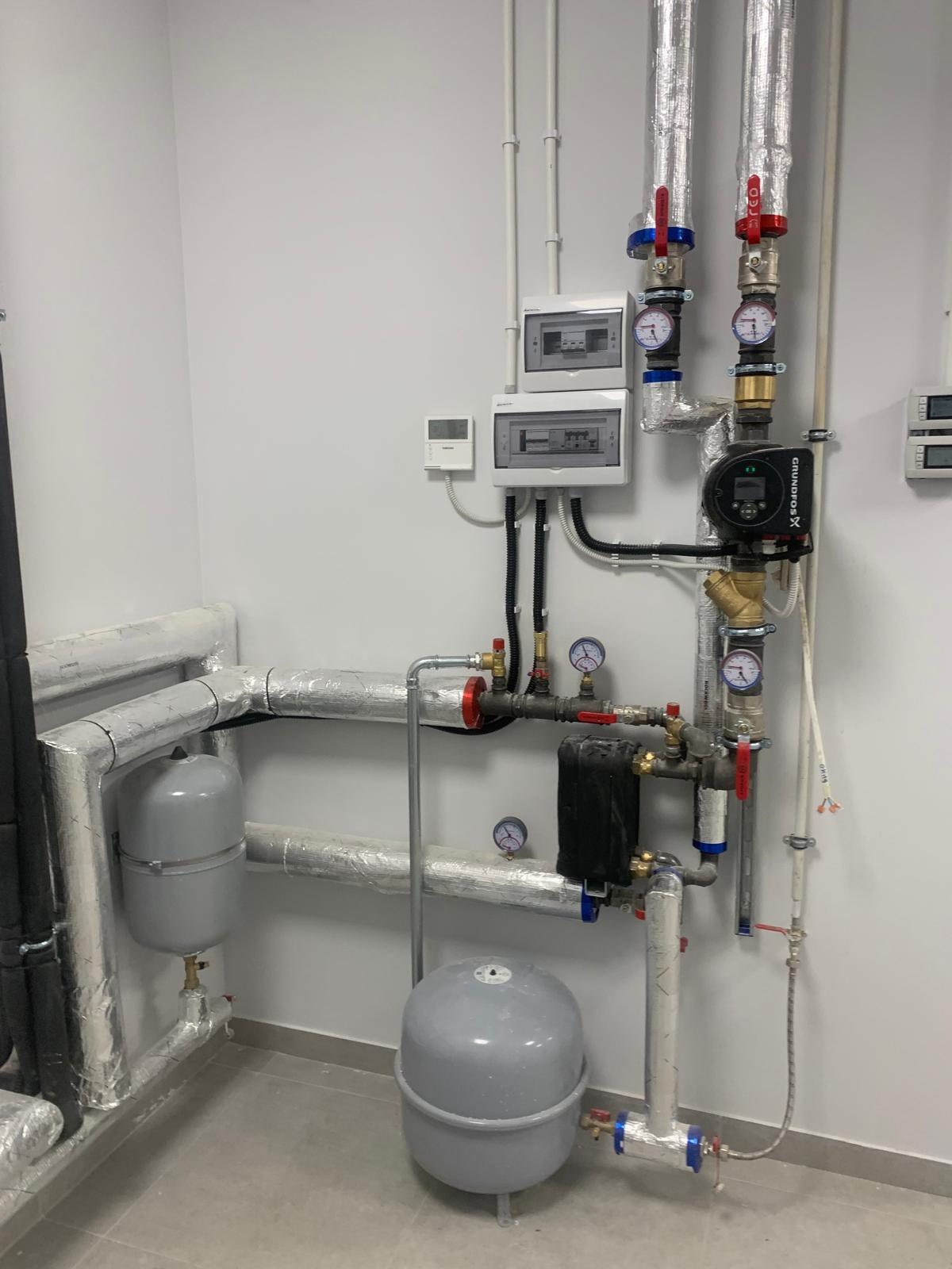 Instalacja grzewcza w kotłowni: rury z izolacją, manometry, zawory, pompy obiegowe, zbiorniki wyrównawcze i sterowniki na ścianie. Nowoczesny system grzewczy.