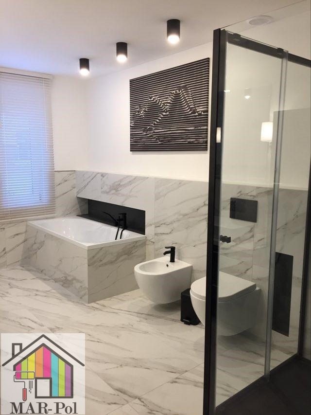 Nowoczesna łazienka z marmurowymi płytkami, czarną armaturą, kabiną prysznicową z czarnymi ramami i abstrakcyjnym obrazem na ścianie.