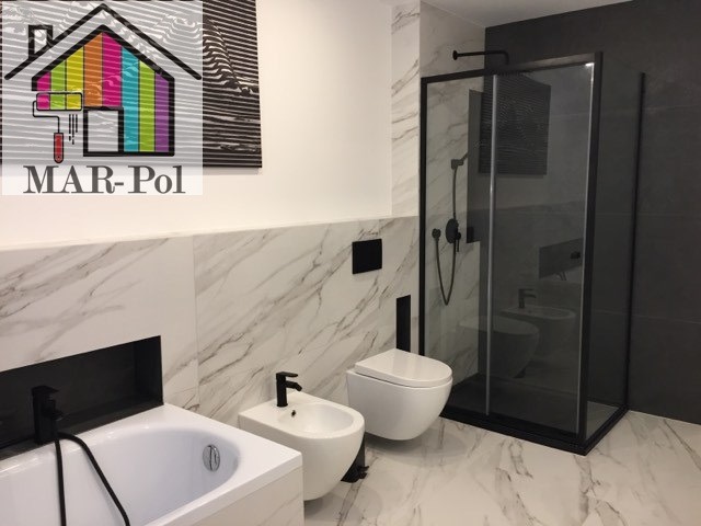 Nowoczesna łazienka z marmurową okładziną, czarną armaturą i kabiną prysznicową typu walk-in, widoczny bidet i toaleta, nad wanną logo firmy MAR-Pol z motywem pędzla i farb.