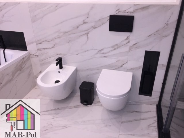 Nowoczesna łazienka w Olsztynie z białymi płytkami imitującymi marmur, wiszącą miską WC, bidetem z czarną armaturą i czarnymi akcesoriami, widok z góry.