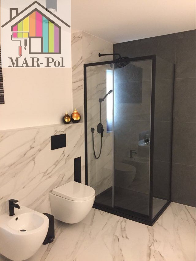 Wykończona łazienka z kabiną prysznicową w czarnej ramie, wiszącą toaletą i bidetem na marmurowej posadzce, dekoracyjnymi złotymi kulami i logo firmy MAR-Pol w rogu.
