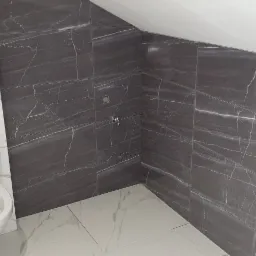 Wykończona łazienka na poddaszu z toaletą podwieszaną i szarymi płytkami imitującymi marmur na ścianach, oraz białymi płytkami na podłodze.