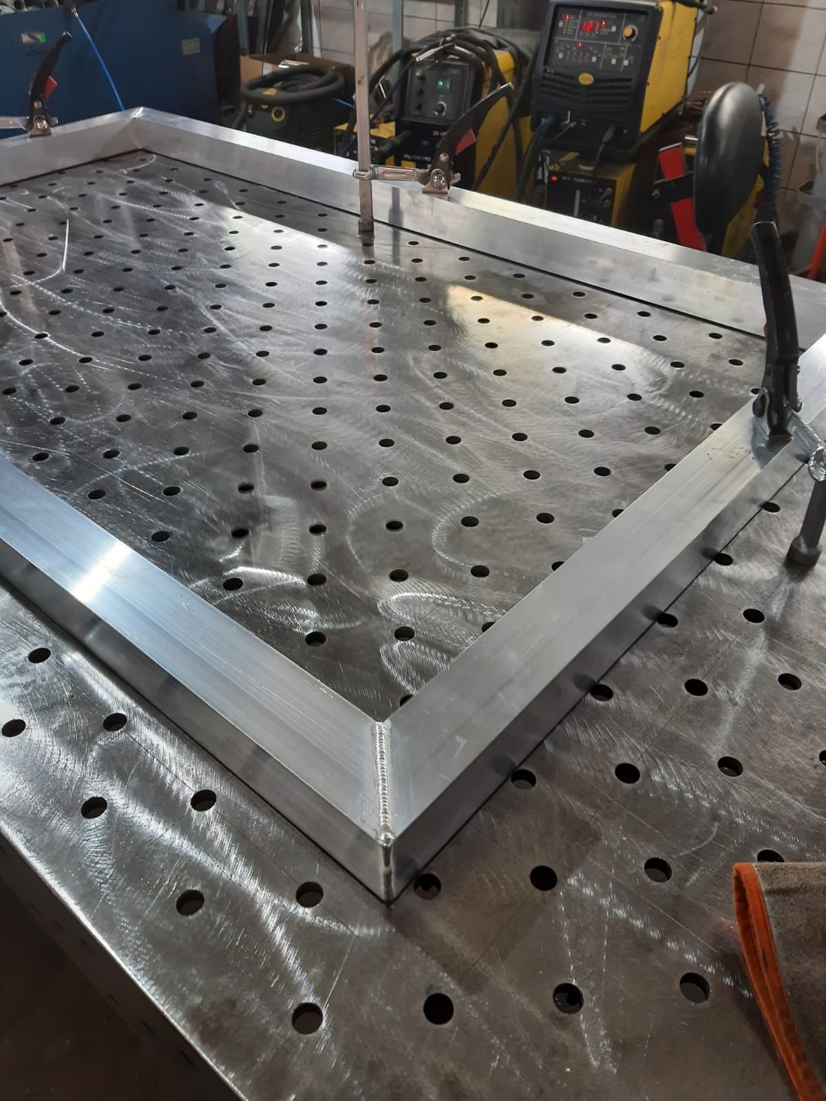 Spawana rama z profili aluminiowych na perforowanym stole spawalniczym, widoczne ślady po spawaniu i mocowania.