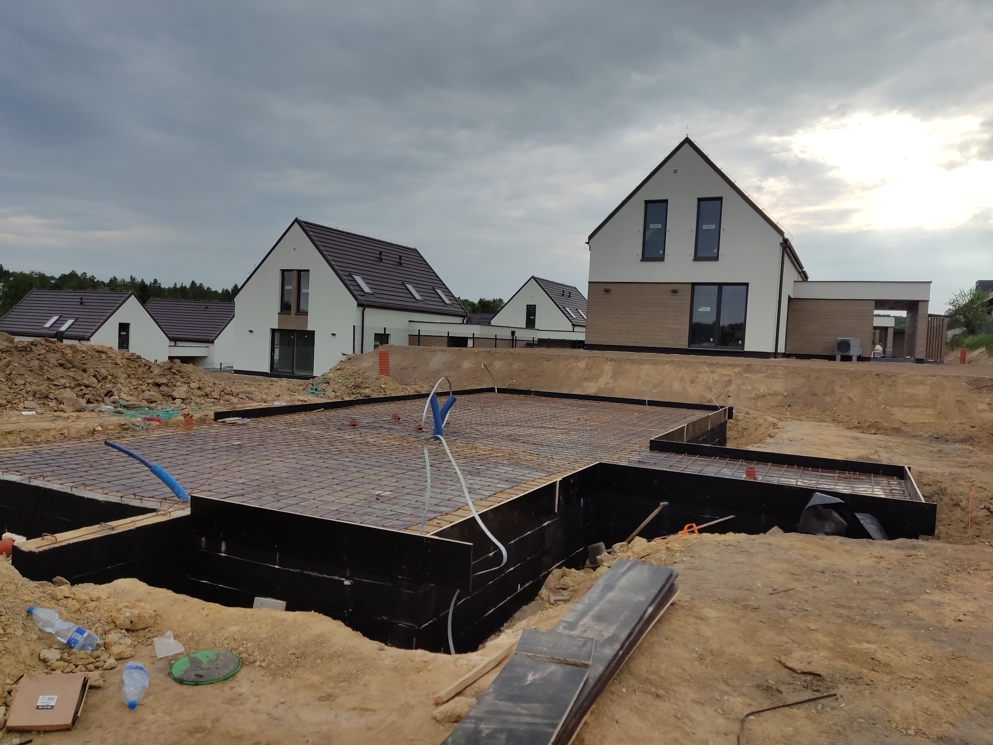 Zbrojenie fundamentów pod budowę kilku nowoczesnych domów jednorodzinnych na osiedlu, widoczne szalunki i wystające rury instalacyjne.