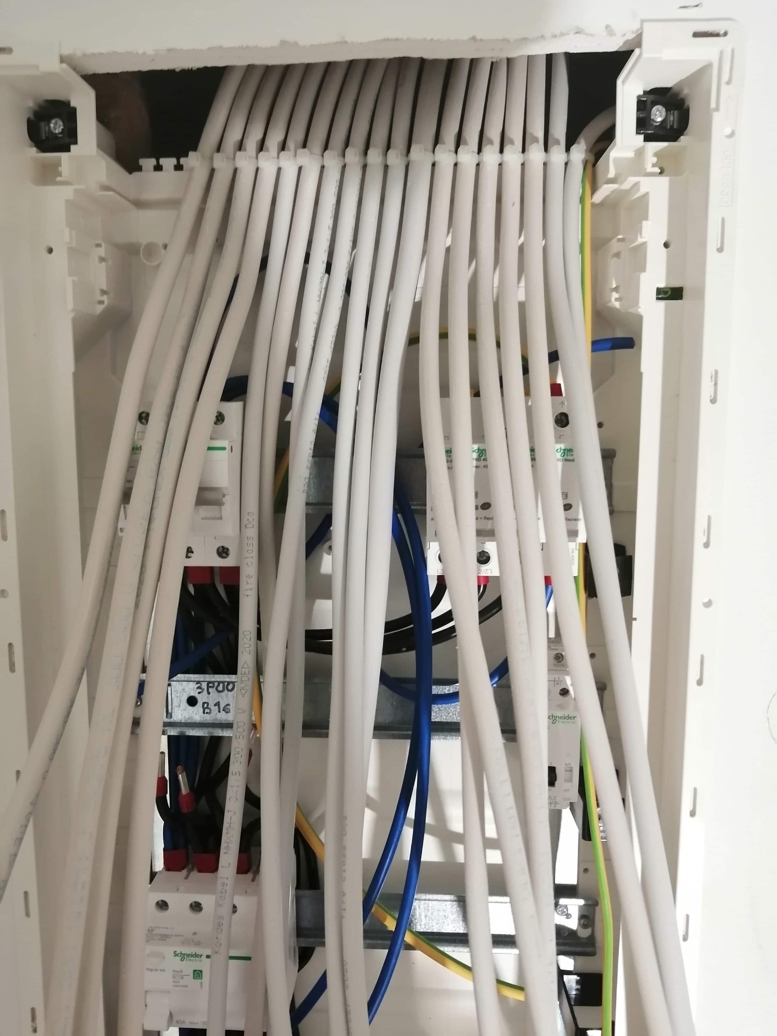 Rozdzielnica elektryczna z białymi przewodami w nowym budynku w Sławnie, widoczne bezpieczniki i kable różnych kolorów.