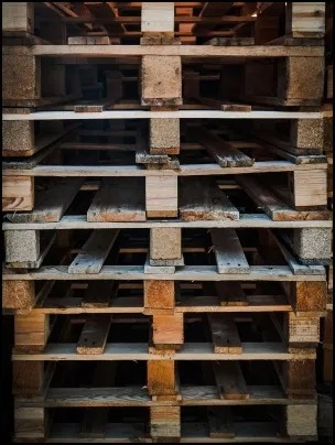 Stos drewnianych palet euro, widoczne ślady użytkowania i drobne uszkodzenia na powierzchni drewna.