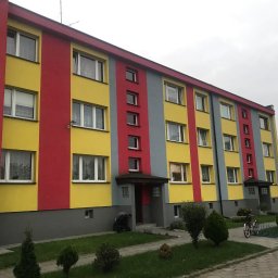 PHU Malbis Leszek Kaleta - Wielobarwny budynek wielorodzinny po renowacji elewacji: żółte, czerwone i szare pasy. Widoczne okna, wejścia i otoczenie z zielenią.