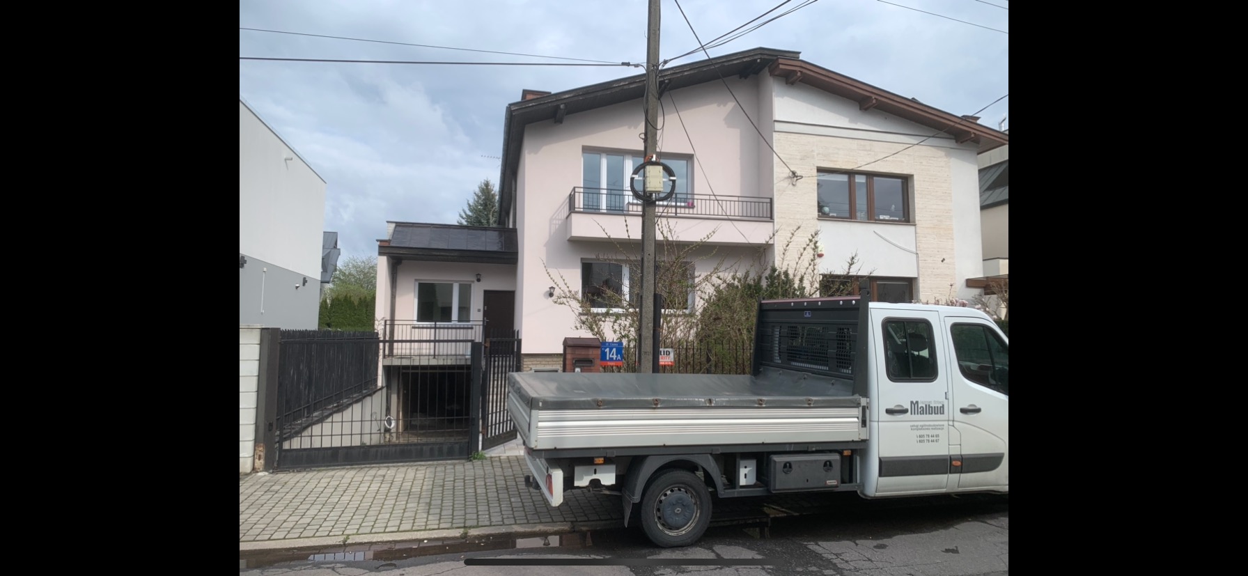 Dom jednorodzinny po renowacji elewacji, z zaparkowanym samochodem dostawczym firmy budowlanej. Widoczne detale architektoniczne i świeża kolorystyka.