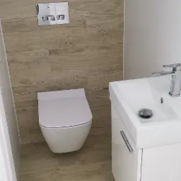 Nowoczesna łazienka z podwieszaną miską WC, umywalką z szafką w kolorze białym oraz płytkami imitującymi drewno na podłodze i ścianie.