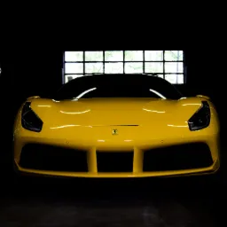 Żółty samochód sportowy Ferrari, widok z przodu w ciemnym garażu z oknem w tle.