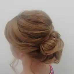 Upięcie ślubne z jasnych włosów, widok z tyłu, kok ułożony z loków, czerwono-niebieska sukienka z wycięciem na plecach.