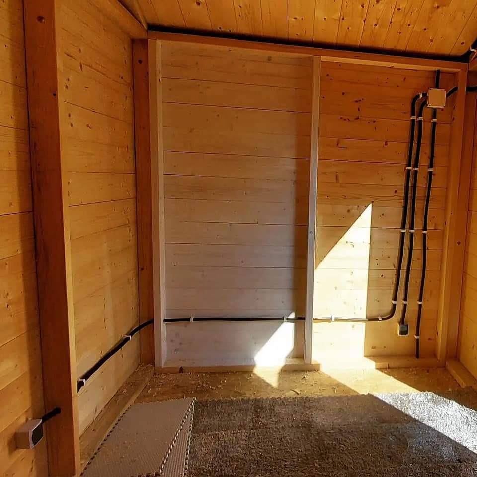 Wnętrze drewnianego pomieszczenia w trakcie montażu instalacji elektrycznej, widoczne kable w peszlach przymocowane do ściany oraz przygotowane miejsce na ściankę działową.