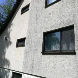 Fragment elewacji domu w Tomaszowie Lubelskim, z widocznym efektem po częściowym odświeżeniu koloru, ukazując różnicę w odcieniach na teksturowanej powierzchni.