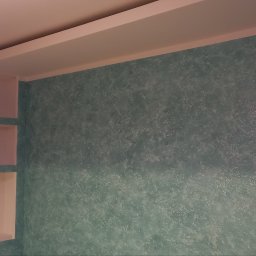 Wagner Tomasz - Wnętrze pokoju z turkusową ścianą o dekoracyjnej, błyszczącej fakturze, wbudowanymi jasnymi półkami i podwieszanym sufitem z oświetleniem.