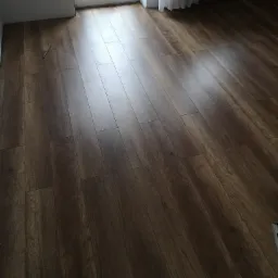 Ułożone panele podłogowe w Tarnowie, imitujące ciemne drewno, z widocznym oknem balkonowym i zasłoną w tle.