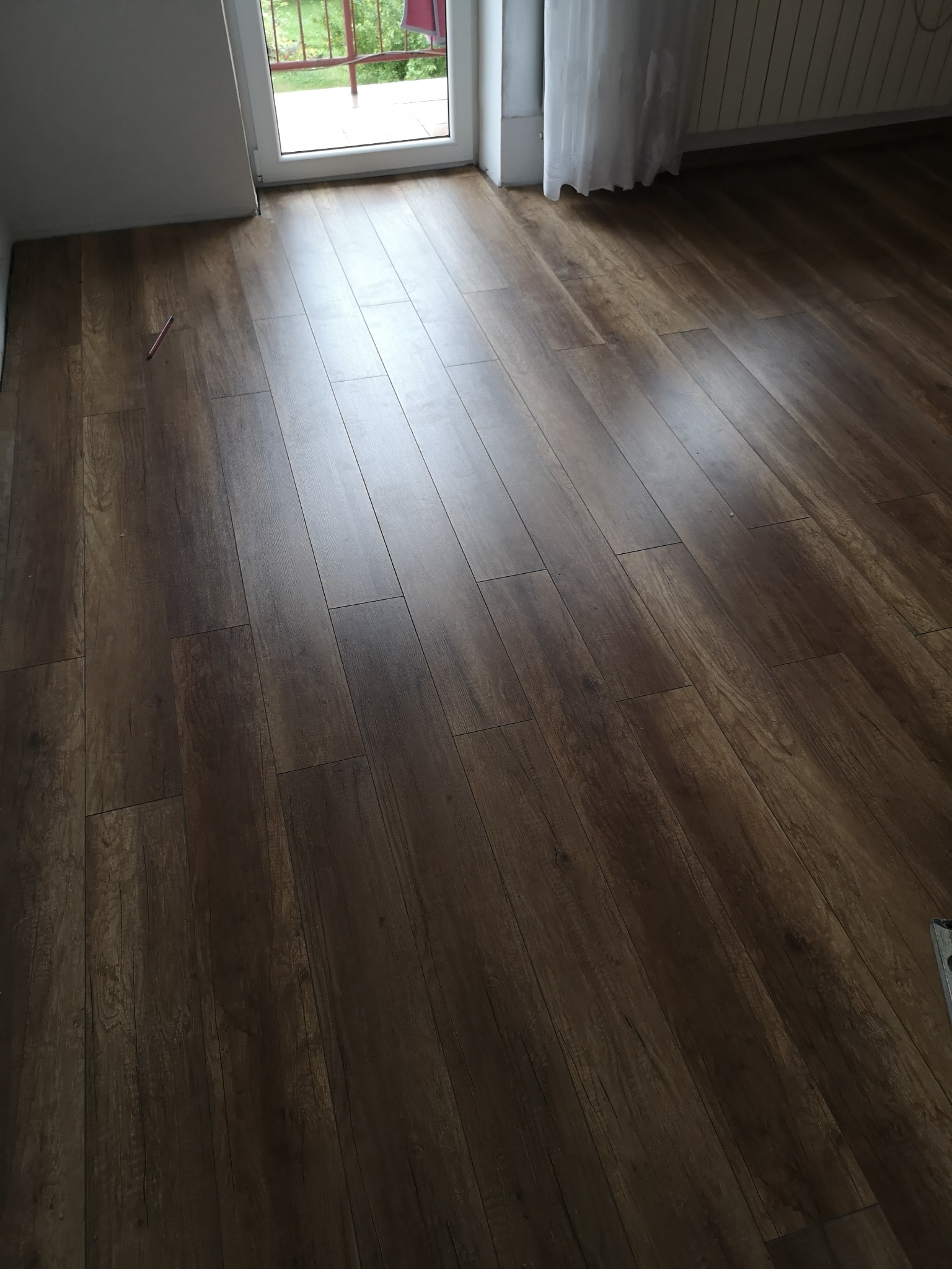 Ułożone panele podłogowe w Tarnowie, imitujące ciemne drewno, z widocznym oknem balkonowym i zasłoną w tle.