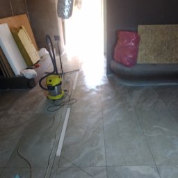 Roksz Michał Usługi Ogólnobudowlane - Ułożone płytki podłogowe w trakcie remontu, widoczny odkurzacz przemysłowy, płyty karton gips oraz materiały budowlane.