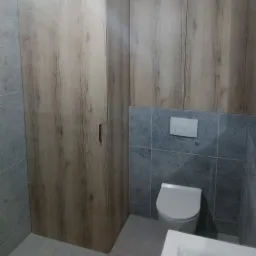 Nowoczesna łazienka z szarymi płytkami, drewnianą zabudową i podtynkową spłuczką WC