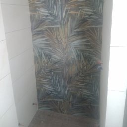 Roksz Michał Usługi Ogólnobudowlane - Fragment ściany w łazience z ułożoną glazurą z motywem liści palmowych, sąsiadująca z białą ścianą wykończoną płytkami.