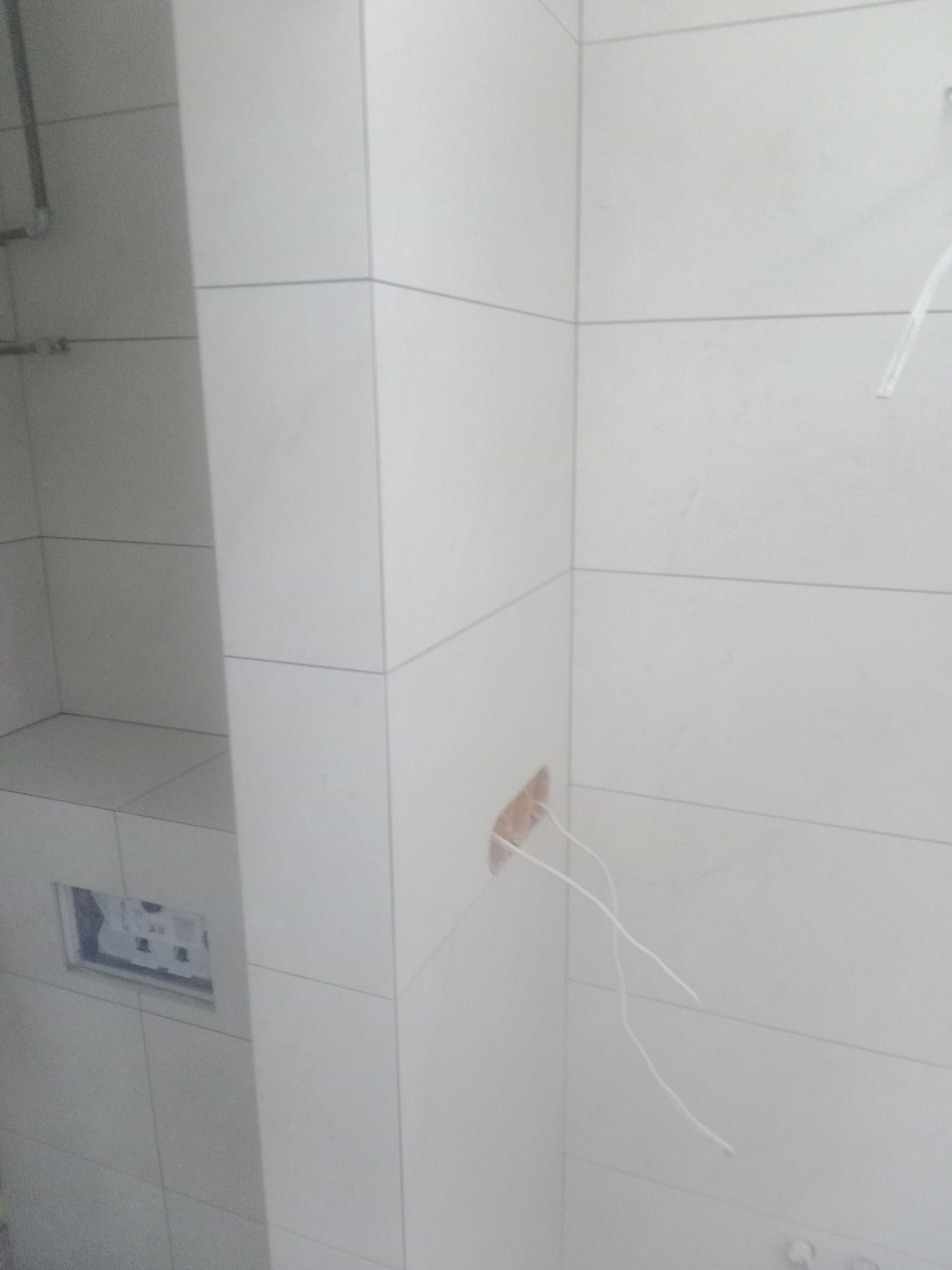 Ściana w trakcie układania płytek w łazience w Bolszewie, widoczne wystające przewody elektryczne i otwór na puszkę podtynkową.