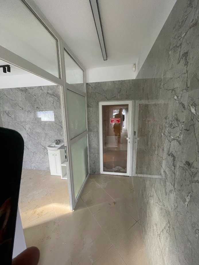 Wykończona łazienka z marmurowymi płytkami, białą umywalką i szklanymi drzwiami. Widoczne detale wykończeniowe i oświetlenie.