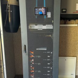 Ozenergy Sp. z o.o. - Szara szafa Lanberg z ekranem dotykowym, obok inwerter Fronius SYMO ADVANCED. Instalacja w pomieszczeniu, widoczny odkurzacz przemysłowy.