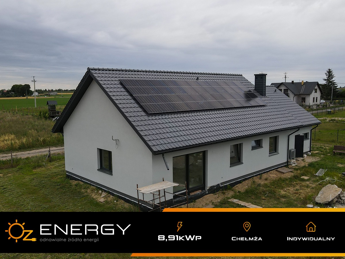 Nowoczesny dom jednorodzinny z panelami słonecznymi na grafitowym dachu, widok z perspektywy lekko podwyższonej, pochmurne niebo.