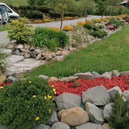 Rodos Tour - Ogród z kamieniami, roślinami i czerwoną korą, z pracownikiem i samochodem dostawczym w tle.