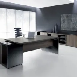 Nowoczesne biuro z ciemnobrązowym biurkiem na wymiar, ciemnoszara ściana i biała podłoga, laptop na biurku, szafka RTV w tle.