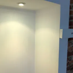 Wnęka w ścianie z oświetleniem punktowym, świeżo pomalowana na biało, sąsiadująca z fragmentem ściany z czerwonej cegły.