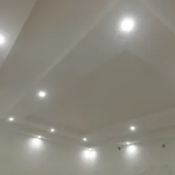 Białe ściany i sufit z dekoracyjnymi wgłębieniami i punktowym oświetleniem LED, widoczne lekkie niedoskonałości wykończenia.