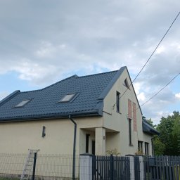 Hydrodynamiczny JAKUB SUROWANIEC - Dom jednorodzinny po renowacji z ciemnym dachem i jasną elewacją, widoczny z boku, z fragmentem rusztowania i drabiny. W tle żółty samochód dostawczy.