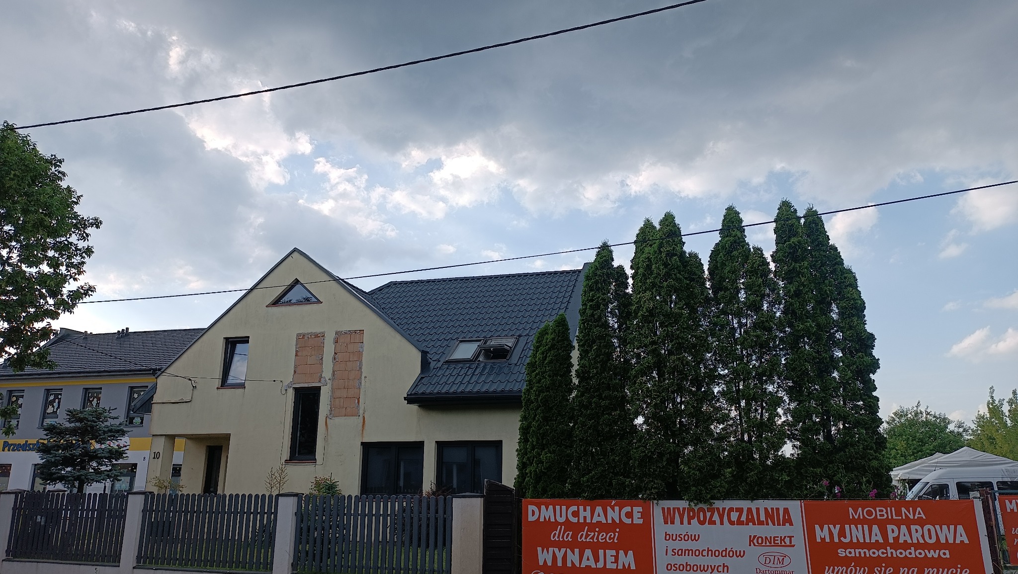 Dom jednorodzinny w trakcie prac elewacyjnych, z widocznymi fragmentami muru przed ociepleniem. Nowy dach z oknami połaciowymi. Tło: pochmurne niebo.