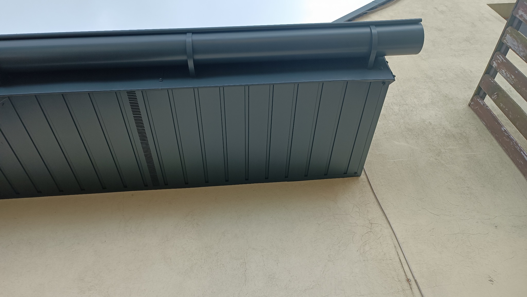 Szczegółowe ujęcie nowej, ciemnej podbitki dachowej z wentylacją, zamontowanej przy jasnej elewacji budynku w Łodzi. Widoczny fragment rynny i drewnianej konstrukcji.