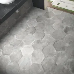 Ułożona szara, heksagonalna glazura pod umywalką w łazience, widoczne zabezpieczenia podłogi przed uszkodzeniem.