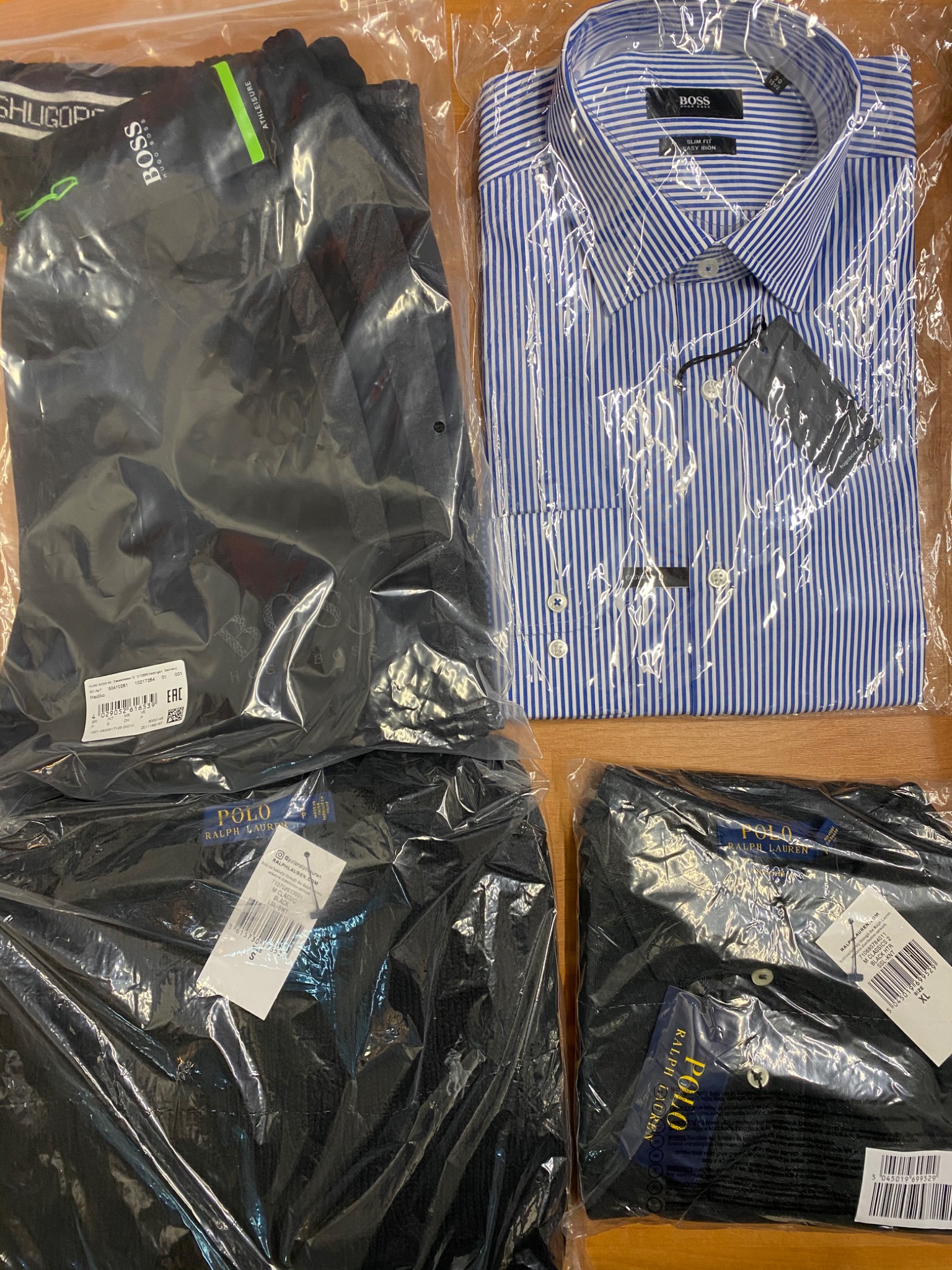 Nowe ubrania markowe w foliowych opakowaniach na drewnianym tle z Raciborza: koszula w paski Boss i spodnie oraz koszulki polo Ralph Lauren z widocznymi etykietami.