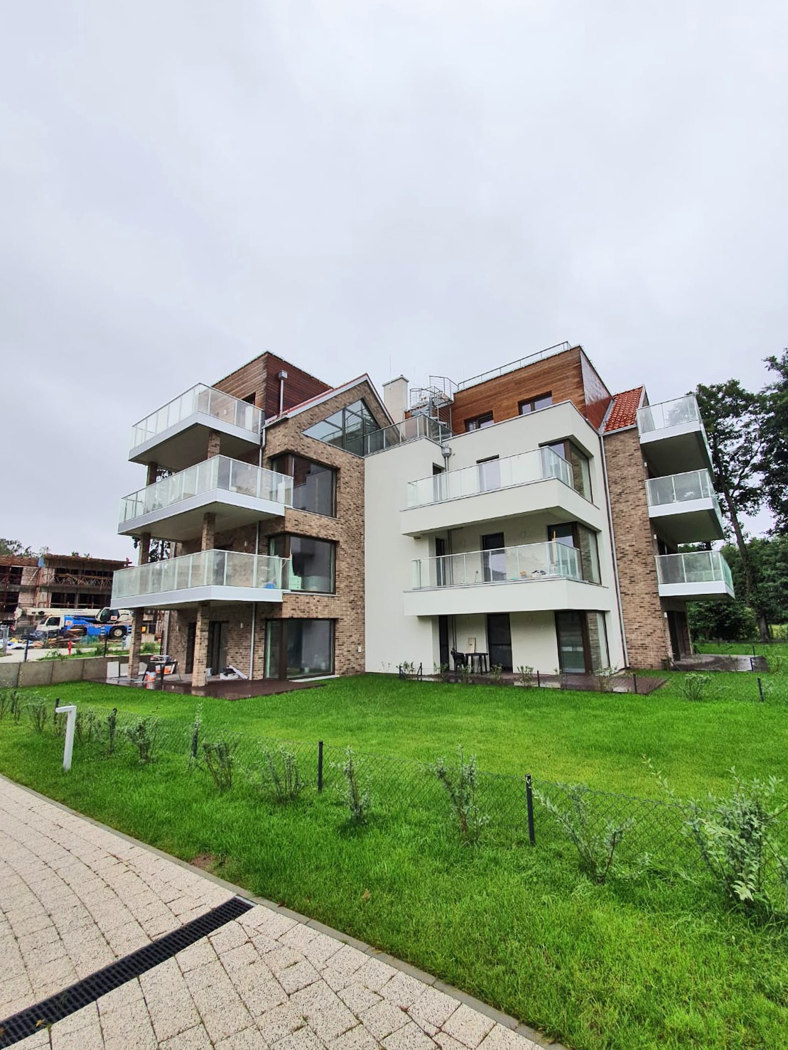 Nowoczesny budynek apartamentowy z balkonami z balustradami szklanymi, widok z poziomu chodnika na zadbany trawnik i elewację z cegły.