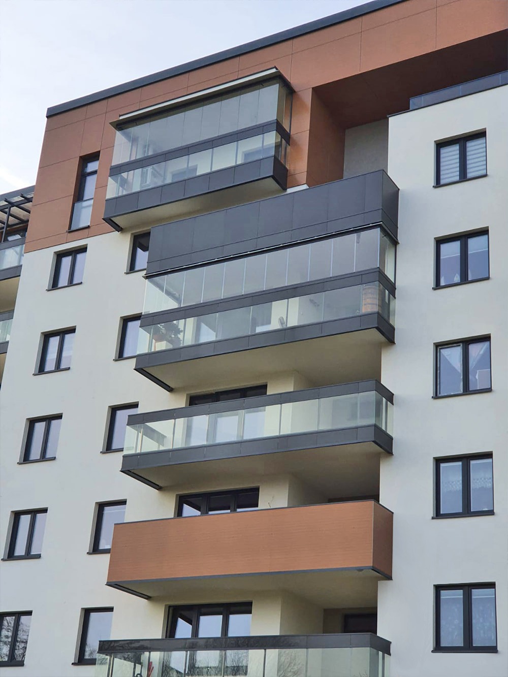 Elewacja budynku mieszkalnego z balkonami z szklanymi balustradami i zabudowanymi loggiami, widok z dołu.