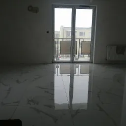 Wykończone wnętrze z błyszczącą, marmurkową podłogą w dużym formacie, odbijającą światło z okna balkonowego, ściany przygotowane do malowania, widoczny grzejnik.