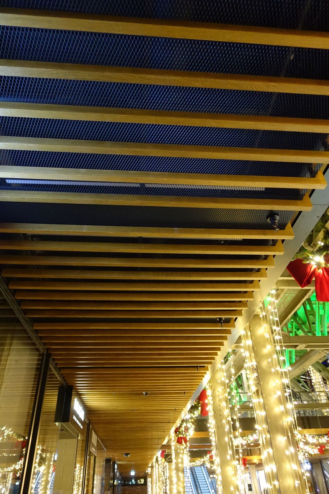 Sufit w centrum handlowym z drewnianymi listwami i metalową siatką, widok z dołu, dekoracje świąteczne w tle.