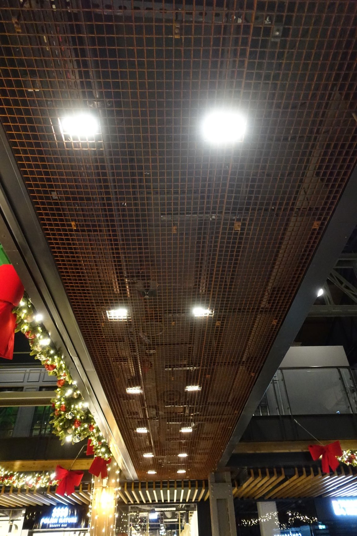 Metalowa konstrukcja sufitowa z siatki z oświetleniem, ozdobiona świątecznymi dekoracjami z czerwonymi kokardami i girlandami z bombkami.