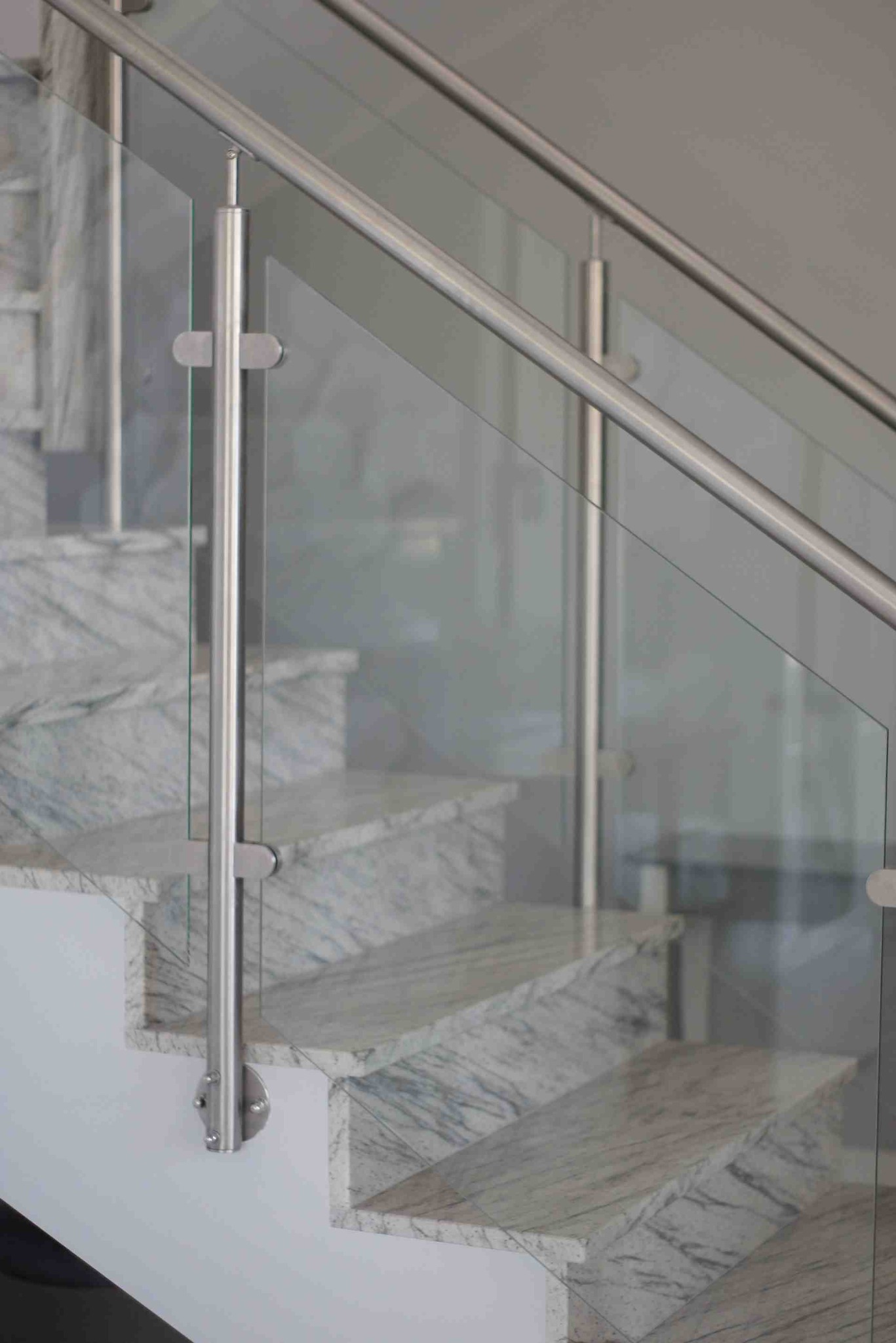 Szklana balustrada ze stalowymi elementami mocującymi, widoczna na tle marmurowych schodów.