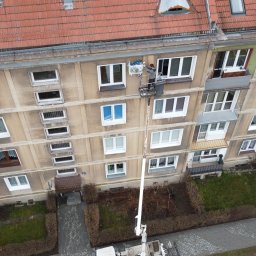 TeslaPV.pl - Fotowoltaika, Klimatyzacja, Pompy Ciepła - Montaż klimatyzacji na wysokości w Oświęcimiu z podnośnika koszowego. Widok z góry na budynek wielorodzinny i pracownika instalującego urządzenie.