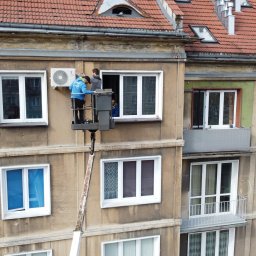 TeslaPV.pl - Fotowoltaika, Klimatyzacja, Pompy Ciepła - Montaż klimatyzatora na elewacji budynku przez dwóch monterów z podnośnika koszowego, widok z góry.