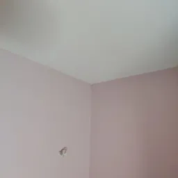 Pomalowane na różowo ściany i biały sufit w rogu pokoju w Warszawie, widoczna puszka instalacyjna bez osprzętu.
