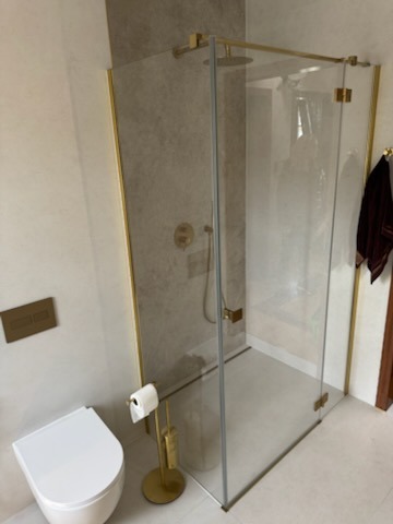 Nowoczesna łazienka z kabiną prysznicową ze złotymi okuciami, wisząca toaleta i stojak na papier toaletowy w kolorze złotym.