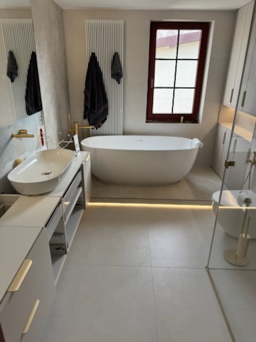 Nowoczesna łazienka w jasnych barwach z wolnostojącą wanną, umywalką nablatową na szafce z szufladami i oświetleniem LED pod wanną.