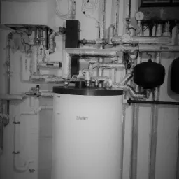 Szaro-białe zdjęcie kotłowni z kotłem Vaillant, licznymi rurami, przewodami i osprzętem, ukazujące złożoność instalacji.