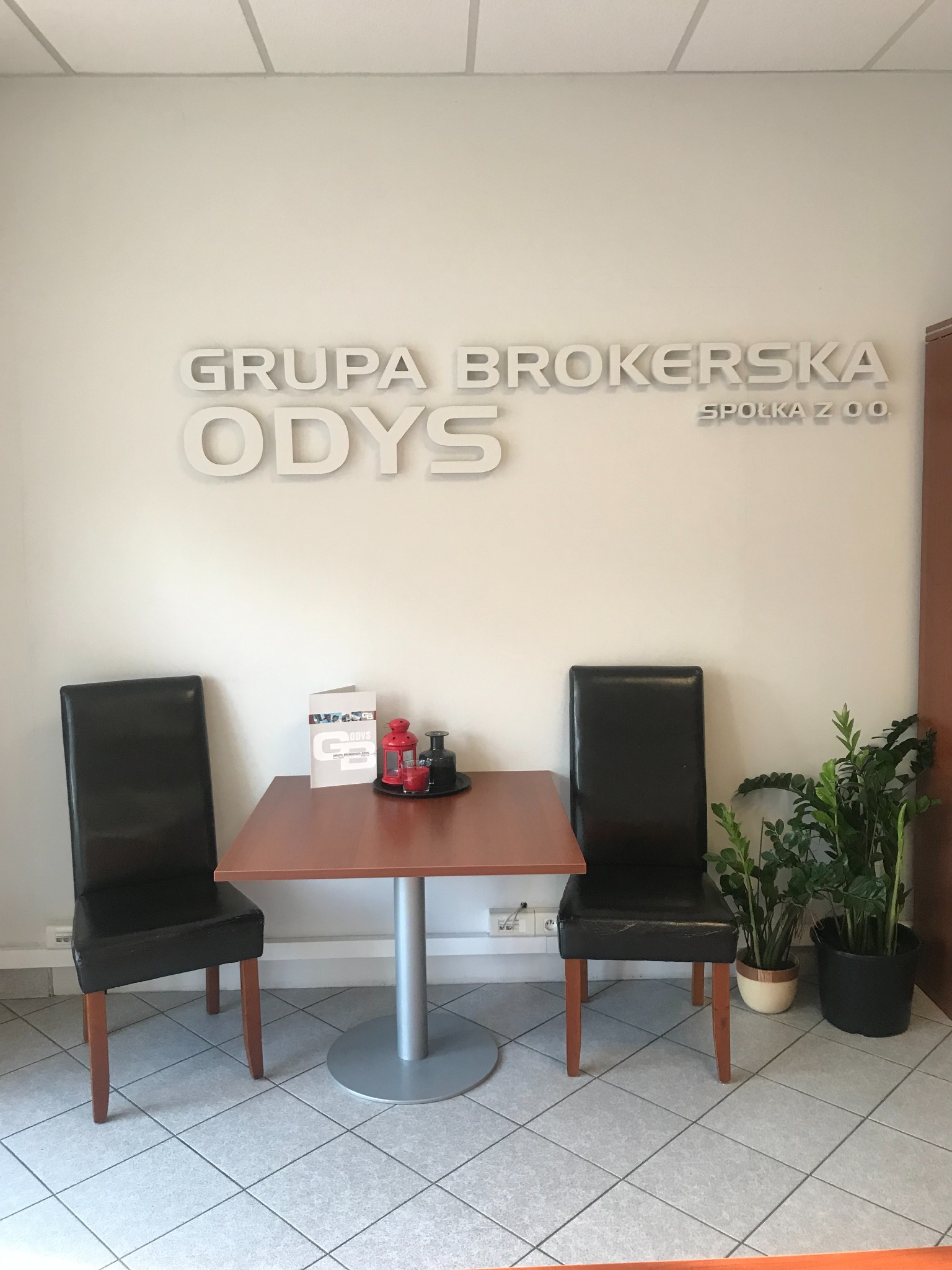 Recepcja biura Grupy Brokerskiej ODYS Spółka z o.o. z dwoma krzesłami, stolikiem z broszurami i roślinami doniczkowymi.