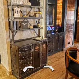 Regał metalowy w stylu industrialnym z półkami i szafkami, eksponujący książki, przyprawy i dekoracje, z logo Harley Davidson na szafkach, oświetlony neonem i listwą LED, na tle drewnianej podłogi...